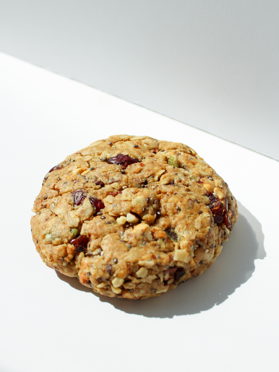 cookie with seeds, nuts and dried berries against a white backdrop with shadows