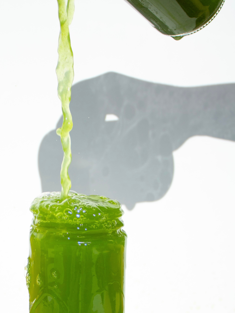 pouring green juice into a glass jar as it bubbles over and splashes against a white backdrop
