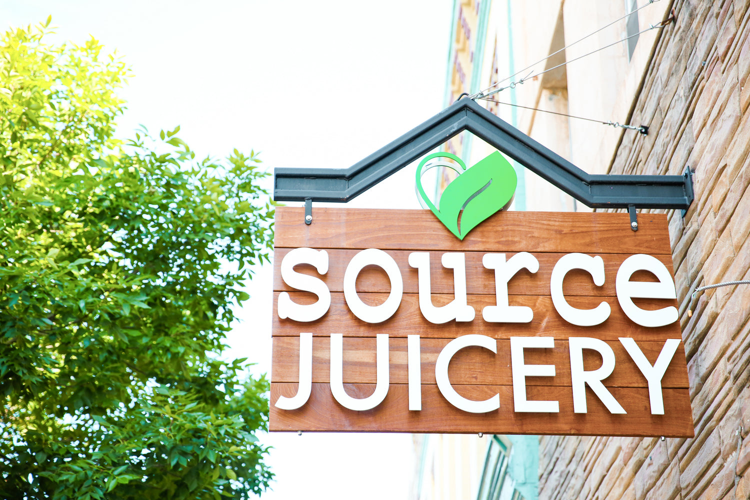 brown wooden sign with white letters spelling source juicery with a green leaf icon