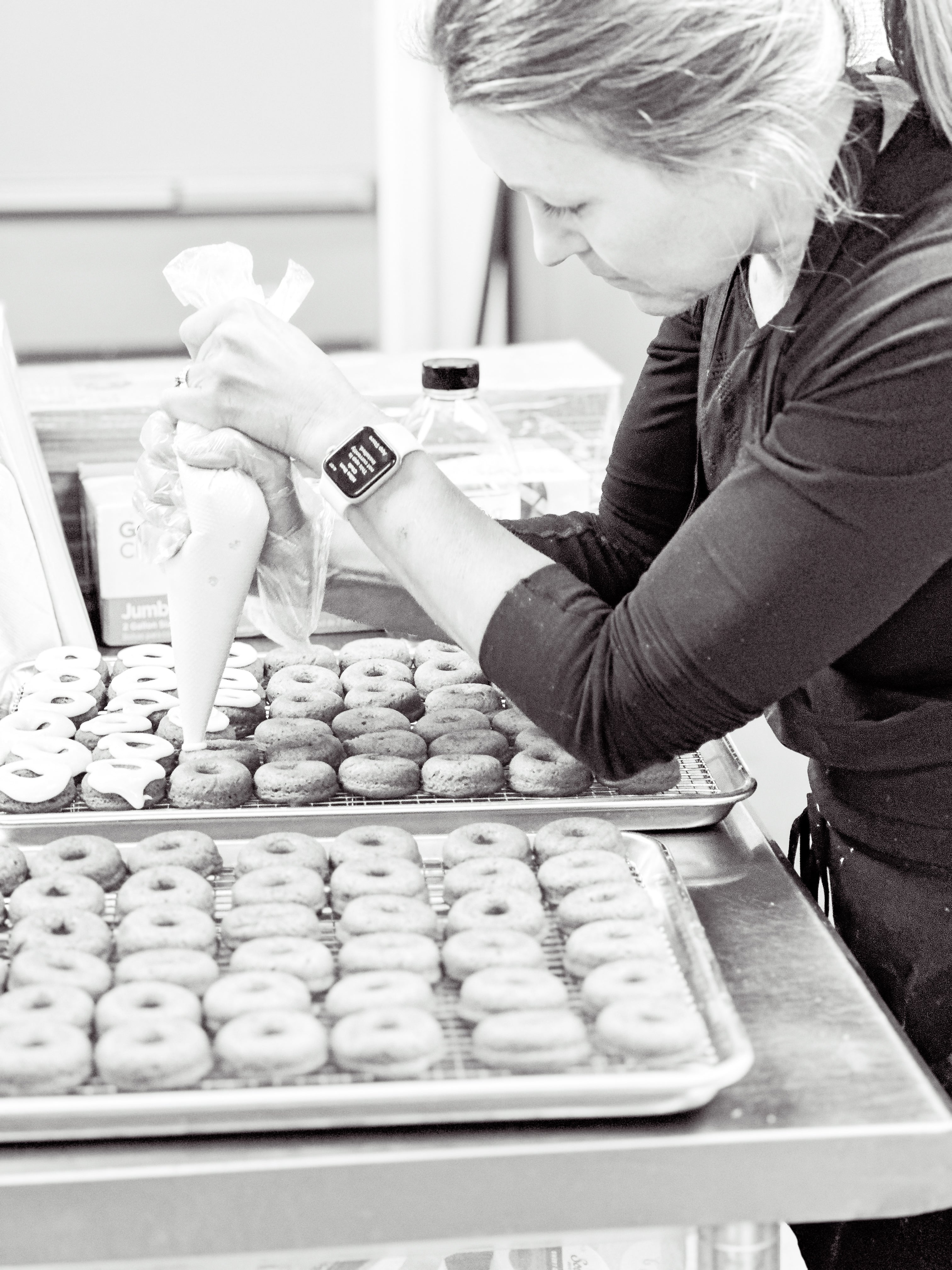woman frosting mini donuts with a piping bag in black and white