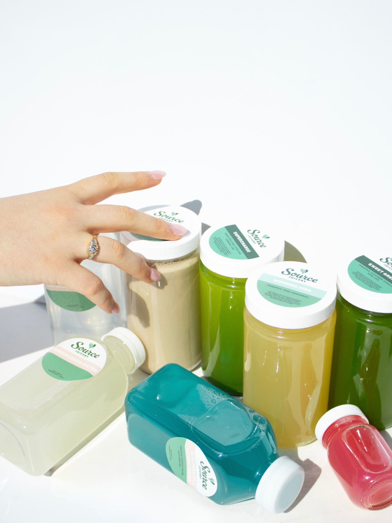 a hand reaching for multiple colored juices against a white backdrop