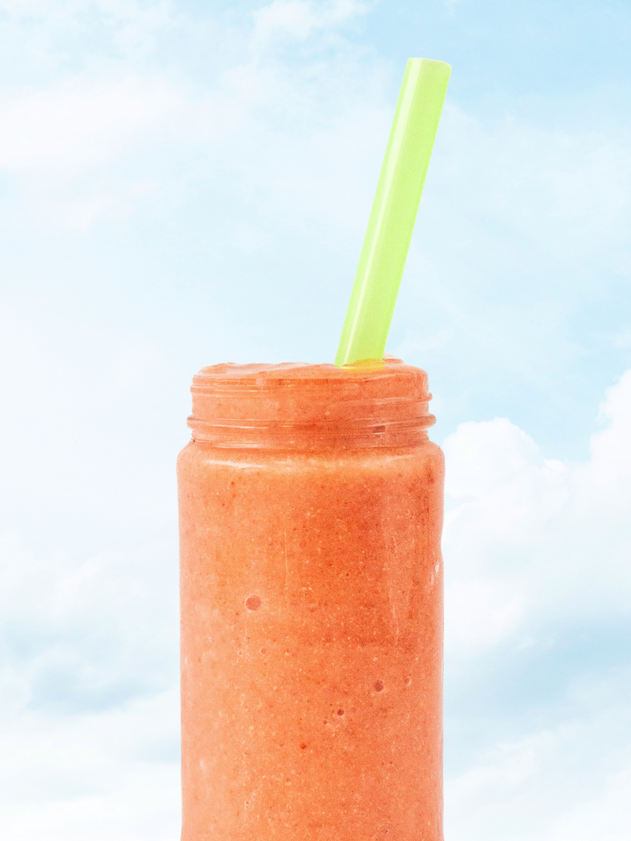 orange smoothie in a glass jar with a lime green straw against a sky backdrop