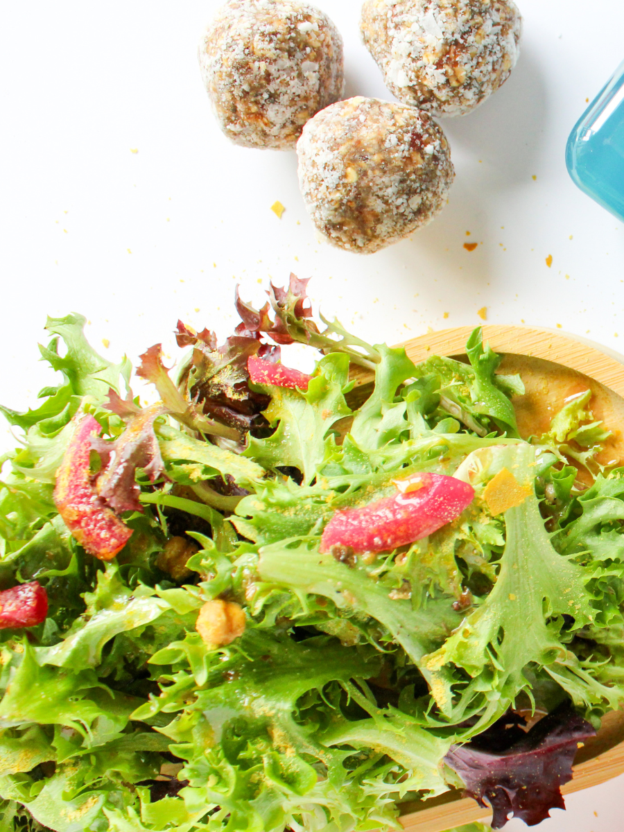 bright green fresh salad with red onions and nutritional yeast next to protein power bites on a white background