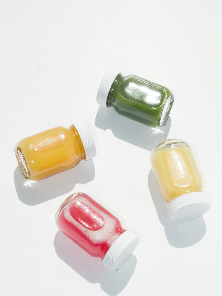 4 small glass jars of wellness shots arranged in a circle in the colors of yellow, green, and pink