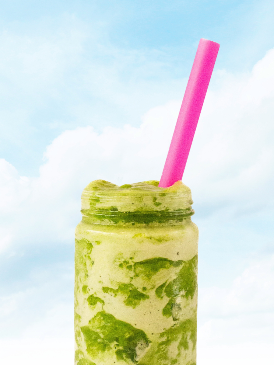 Marbled green and cream smoothie in a glass jar with a hot pink straw against a sky background